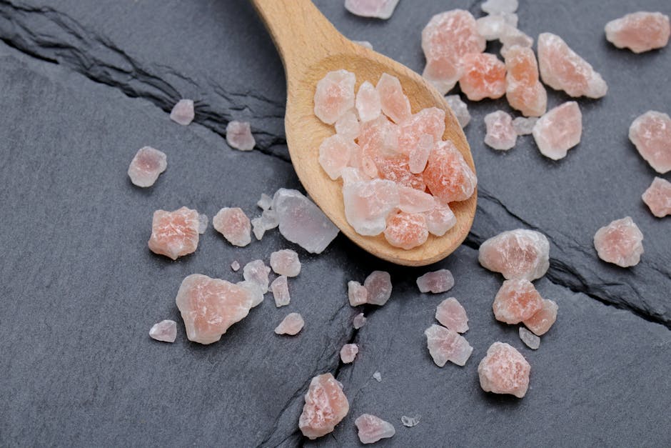 Close-up of Himalayan pink salt crystals on a wooden spoon and slate background, perfect for culinary use.
